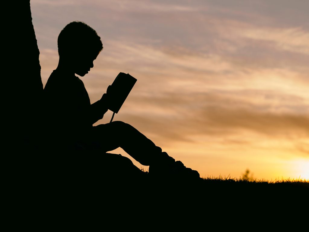 a silhouette of a young person reading a book